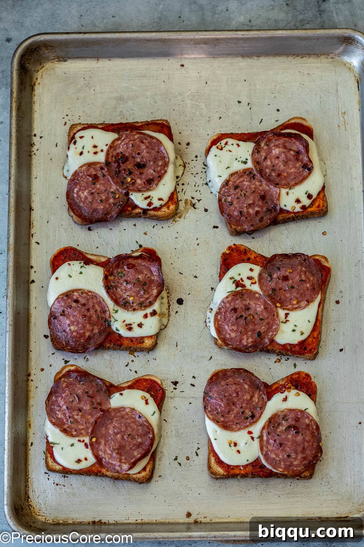 Freshly baked pizza toasts on a baking sheet, with perfectly melted and bubbly cheese.
