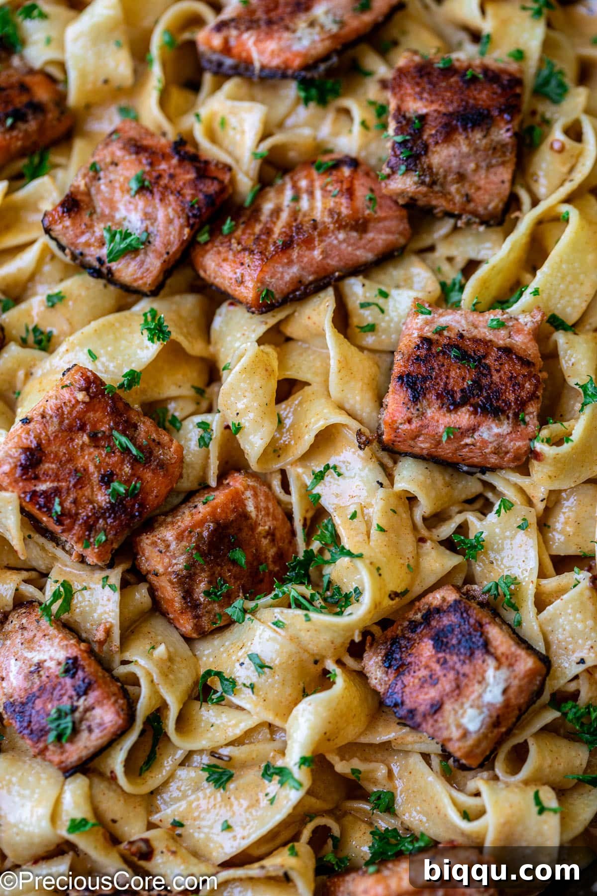 Cajun pasta with creamy sauce and salmon pieces, garnished with herbs.