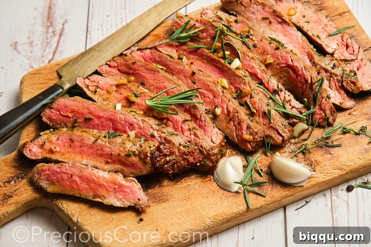 Wide shot of flank steak on cutting board with herbs and garlic.