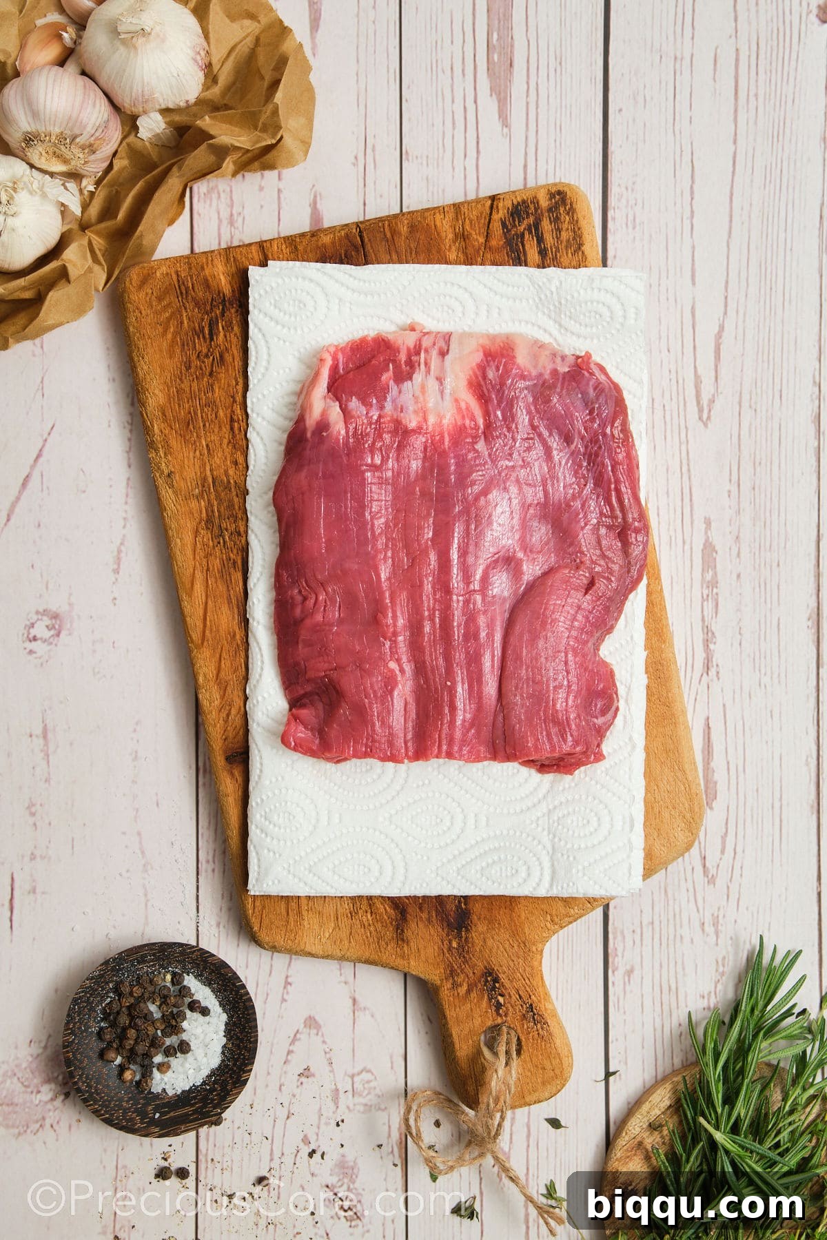 Patting dry flank steak with paper towels for optimal searing.