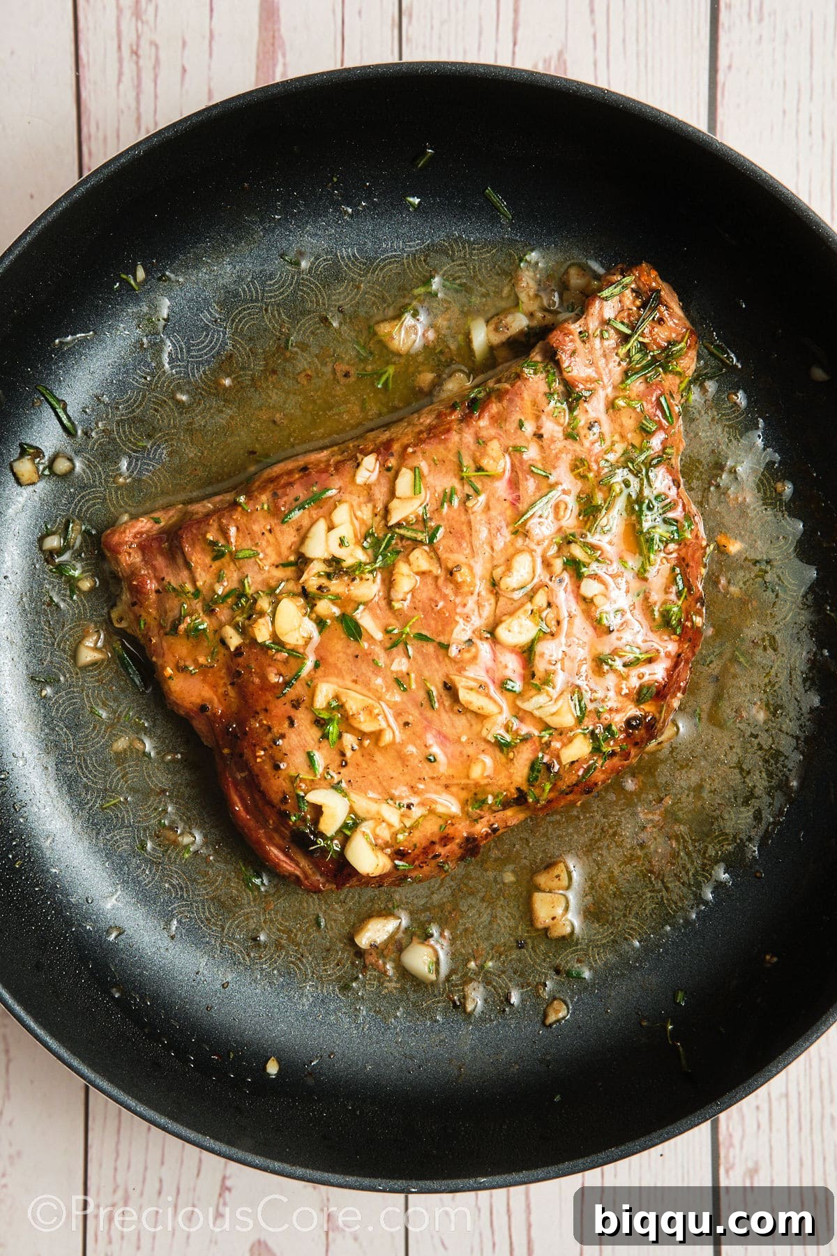 Pan seared flank steak being basted with garlic herb butter sauce.