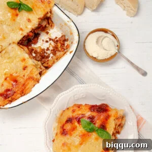 Slice of Lasagna on a plate with a bowl of freshly baked lasagna on the side.