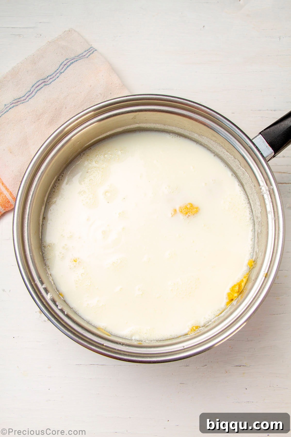 Warm milk being gradually added to the roux in a saucepan, creating a smooth mixture.