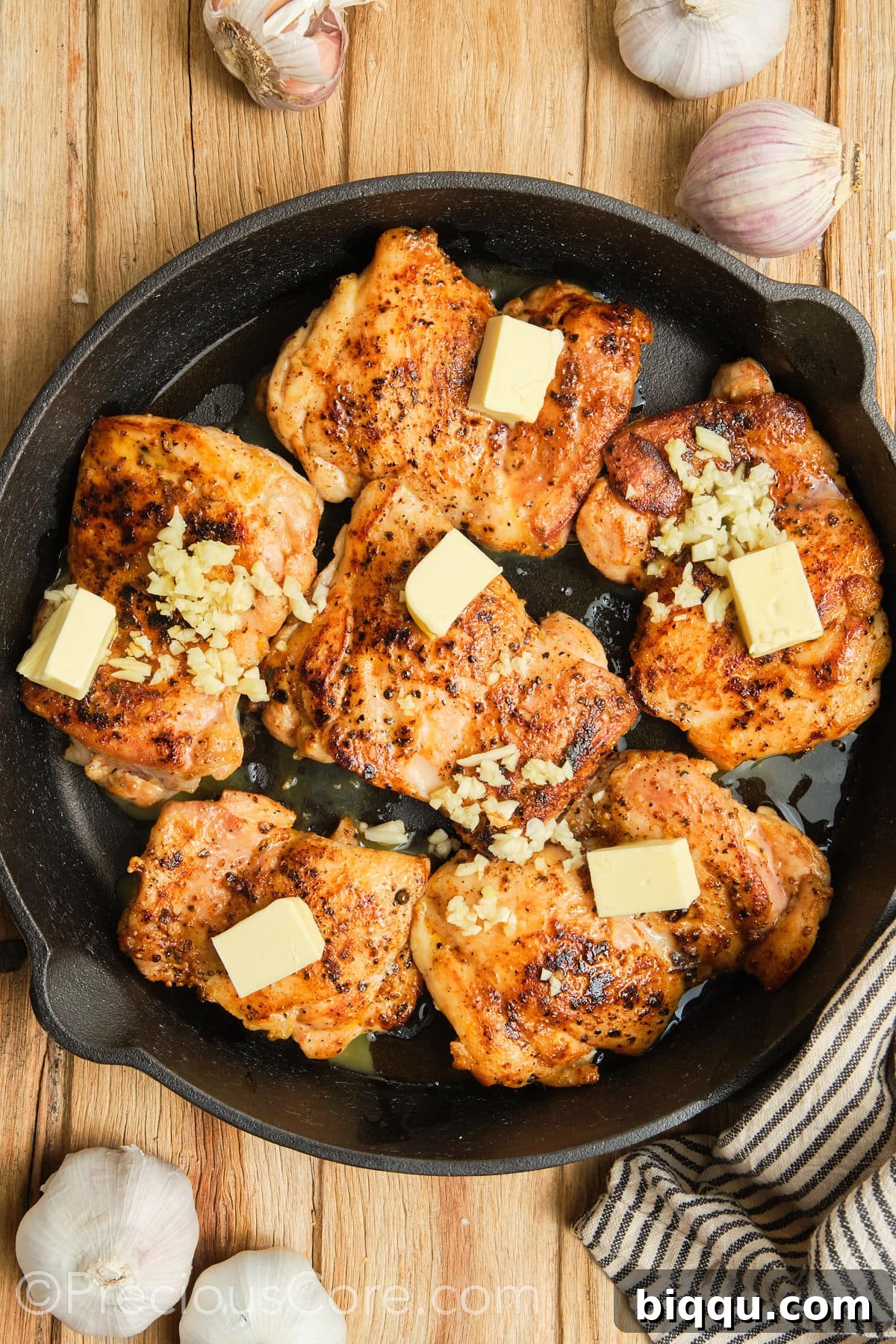 Cubed butter and minced garlic added to a skillet with seared chicken thighs, melting and sizzling.