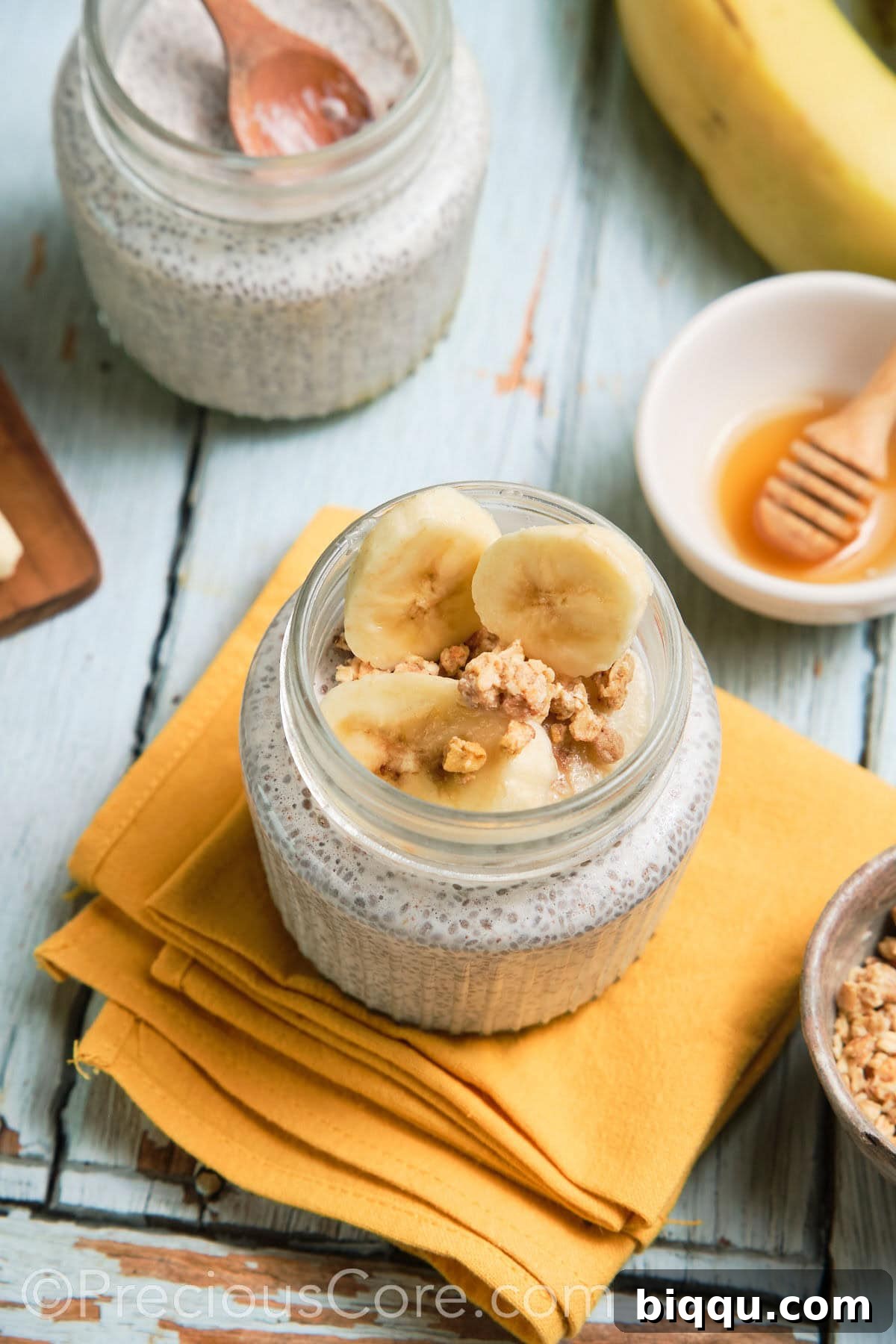 Two glass jars of chia pudding, one topped with berries, the other with banana slices.