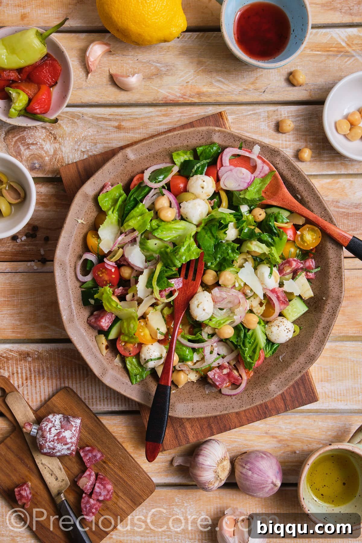 Someone gently mixing the fresh ingredients of an Italian Chopped Salad in a large bowl.