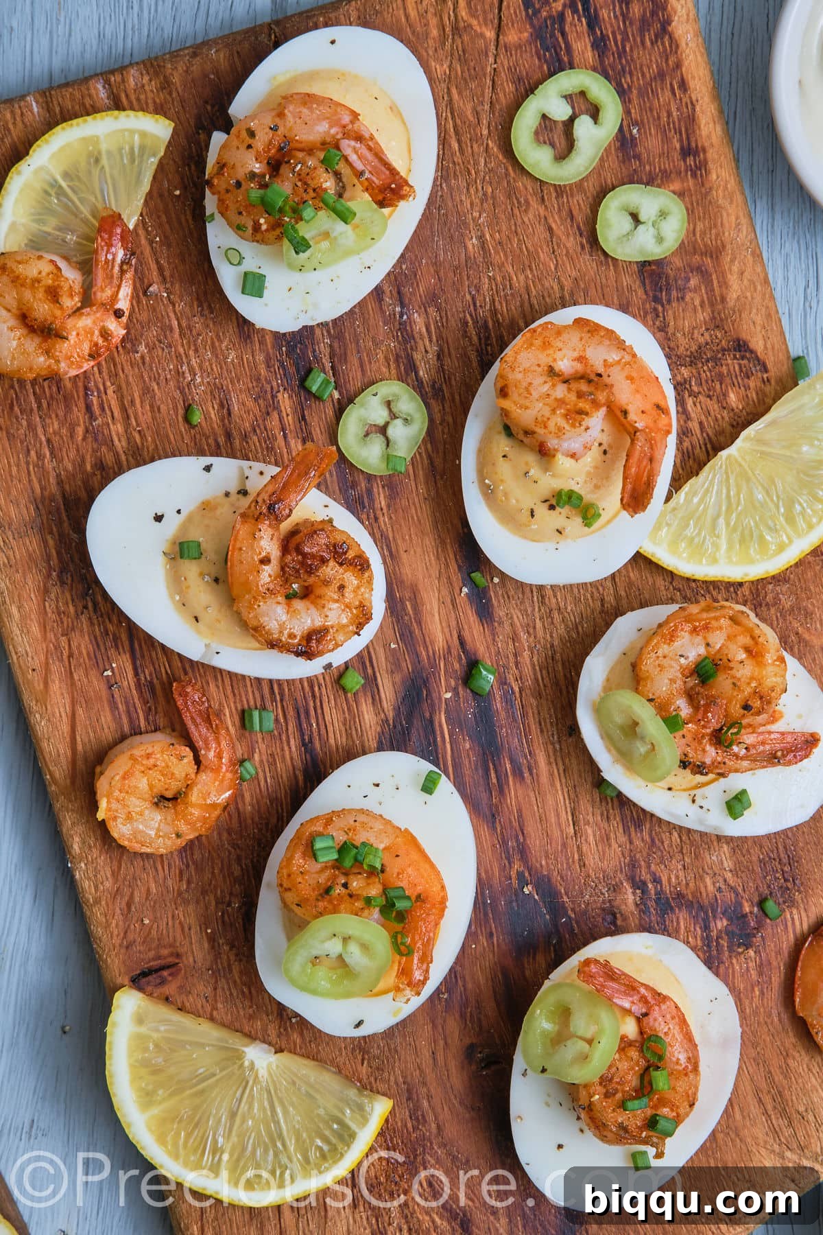 Deviled eggs with Cajun shrimp elegantly arranged on a rustic chopping board, garnished with fresh herbs and lemon slices.