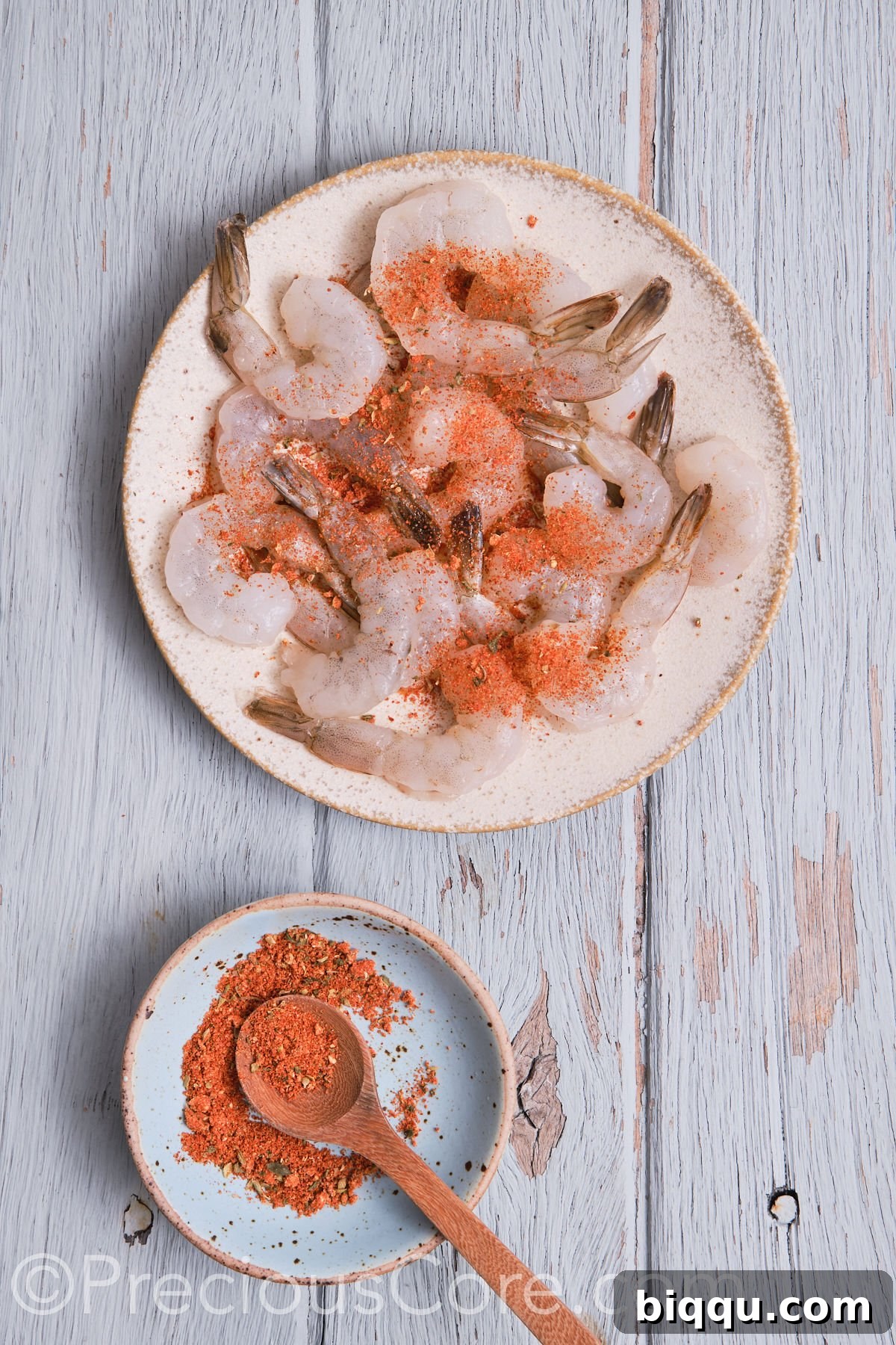 Raw shrimp seasoned with Cajun spices, neatly spread on a plate, ready for cooking.