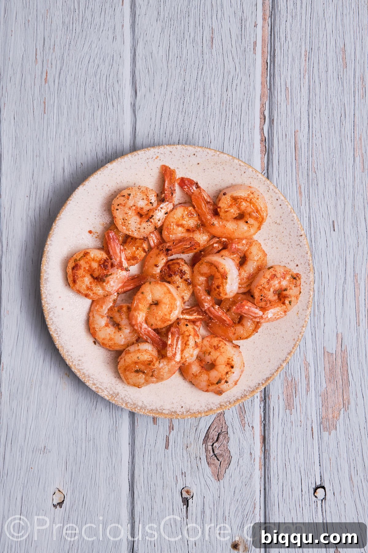 Perfectly cooked Cajun shrimp, vibrant pink and ready to be used as a delicious topping, cooling on a plate.