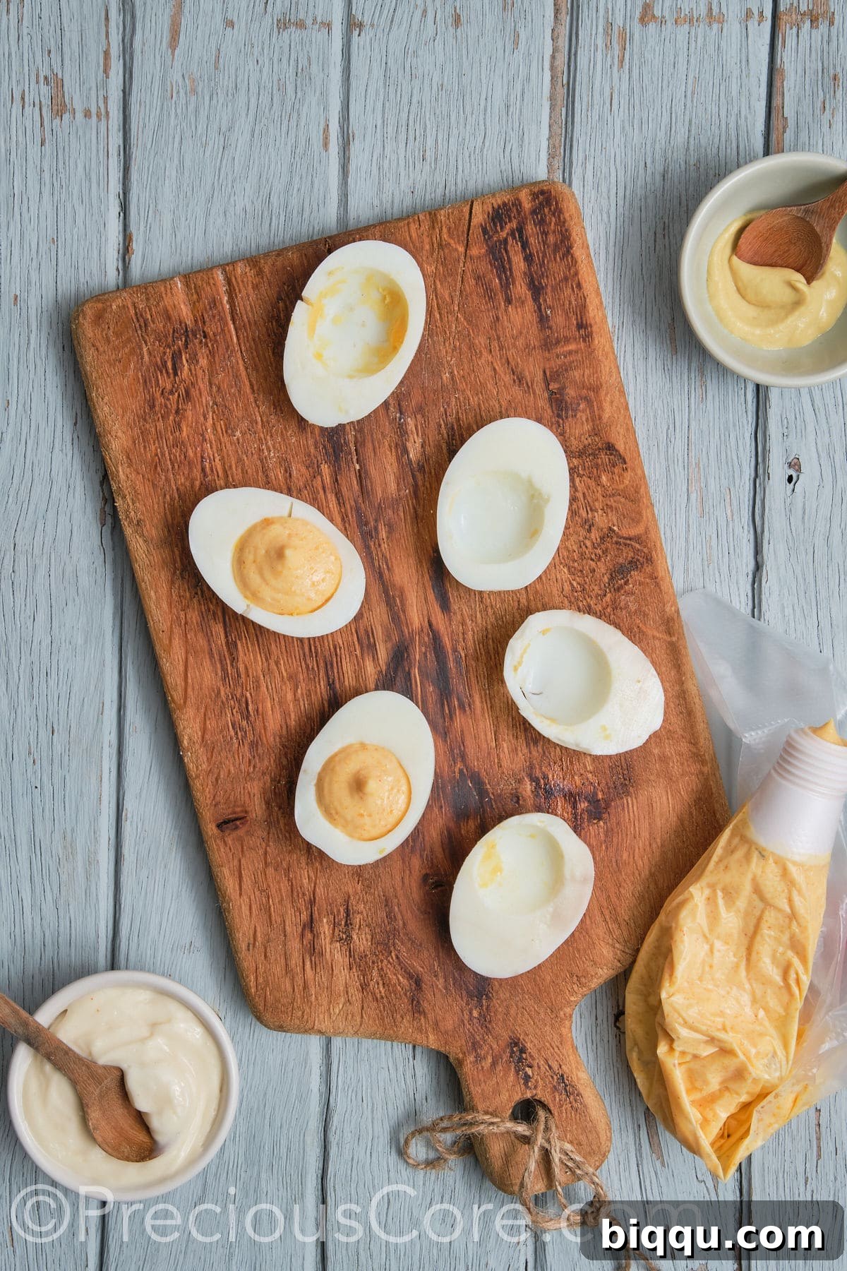 Hollowed-out egg white halves arranged, with a spoon beginning to scoop the creamy yolk mixture into one.
