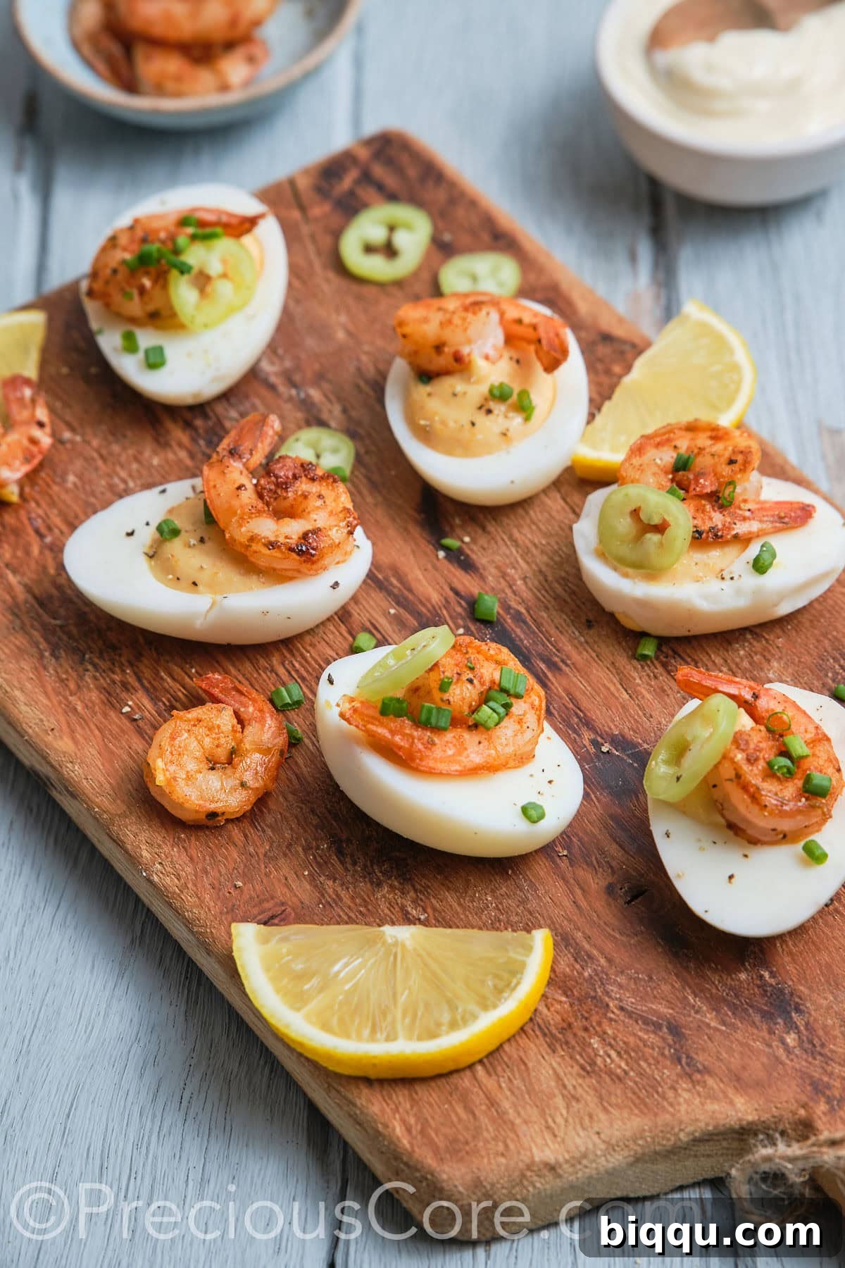 A close-up side view of perfectly crafted deviled eggs, each topped with a vibrant Cajun shrimp and a sprinkle of fresh green chives, artfully arranged.