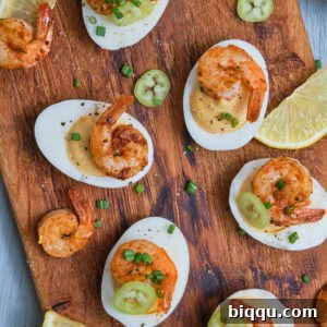 Deviled eggs with Cajun shrimp on a chopping board, garnished with fresh herbs and lemon.