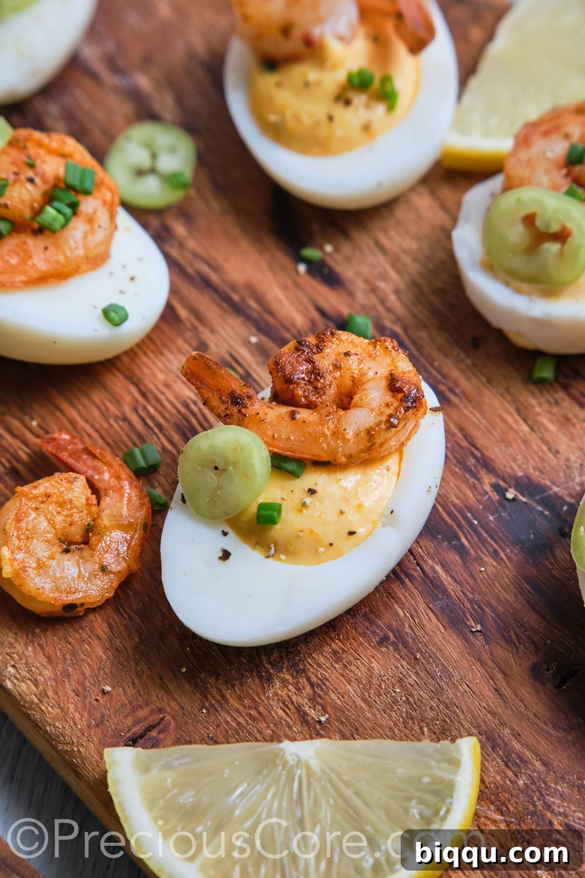 A close-up shot focusing on a single, beautifully prepared deviled egg topped with a succulent Cajun shrimp and a tiny sprig of chive, highlighted against a blurred background.