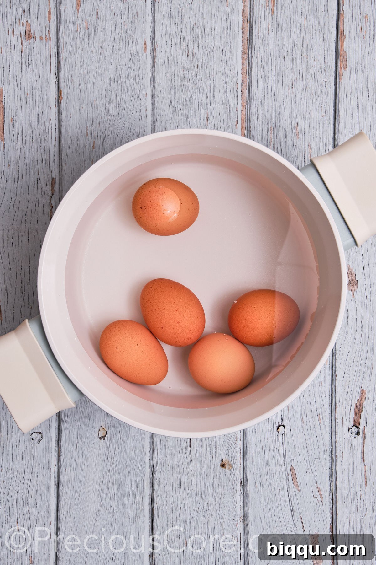 Raw eggs carefully placed in a saucepan, covered with water, ready for boiling.