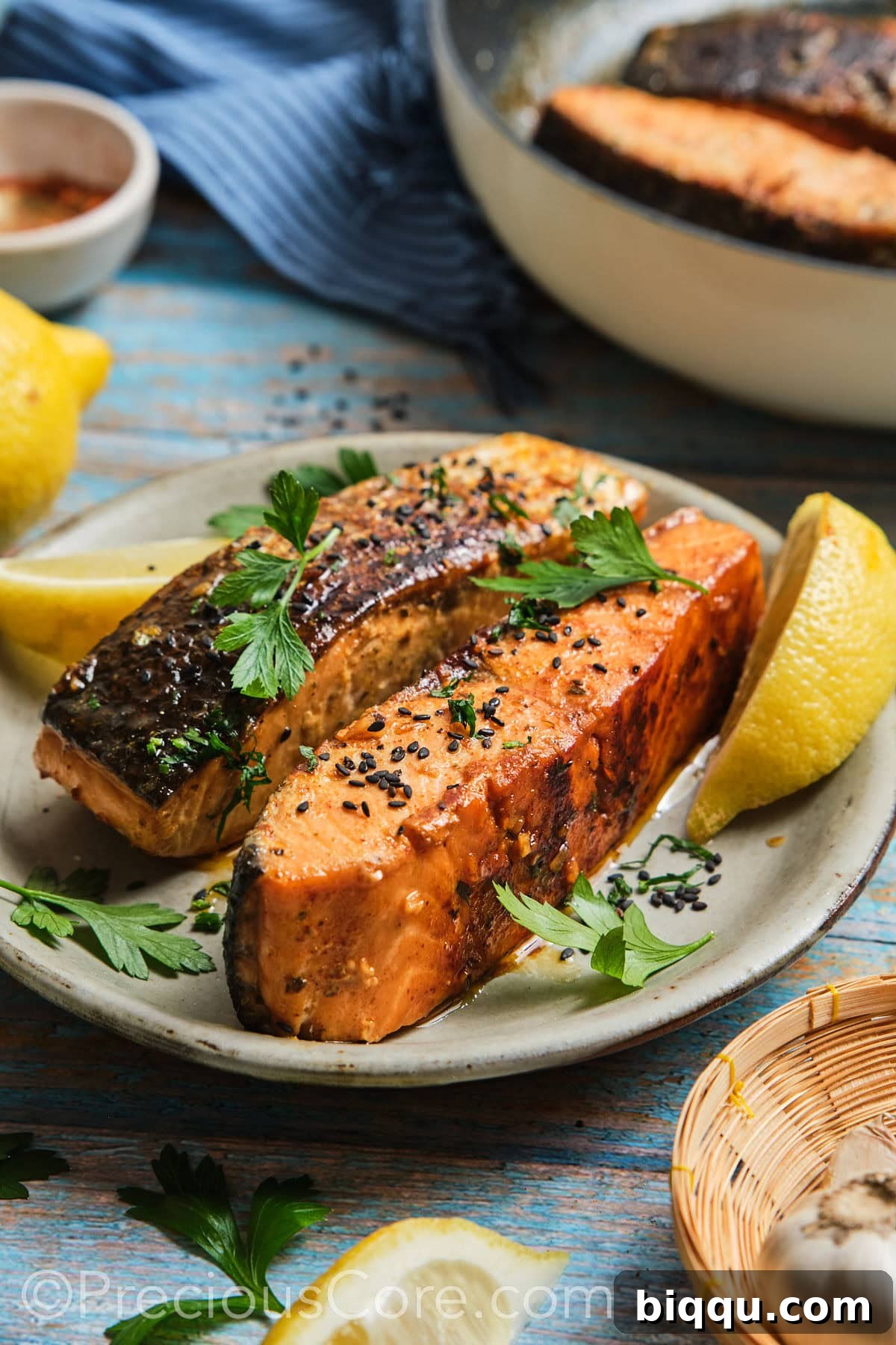 Two glistening cooked salmon fillets, artfully garnished with black sesame seeds, ready to be served.