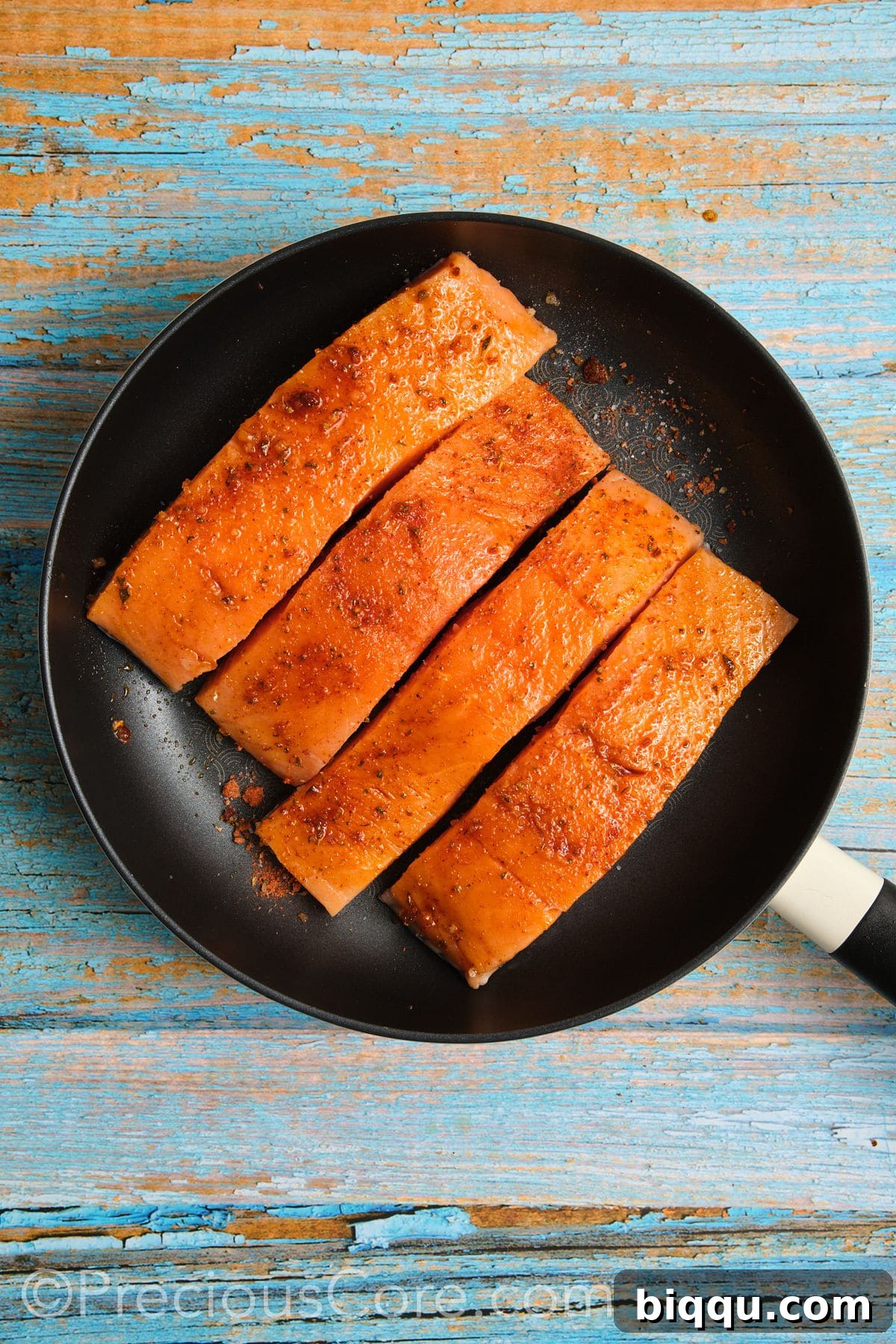 Salmon fillets sizzling in a hot skillet, skin-side down, achieving a perfect sear.