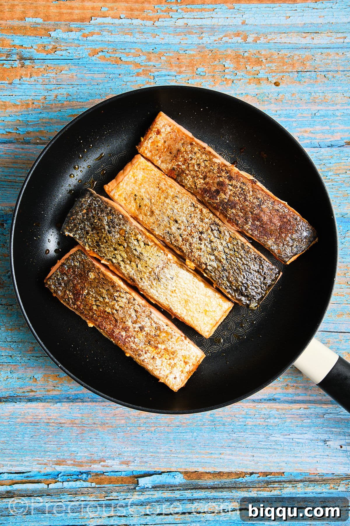 A salmon fillet skillfully flipped in the skillet, now cooking on its flesh side.