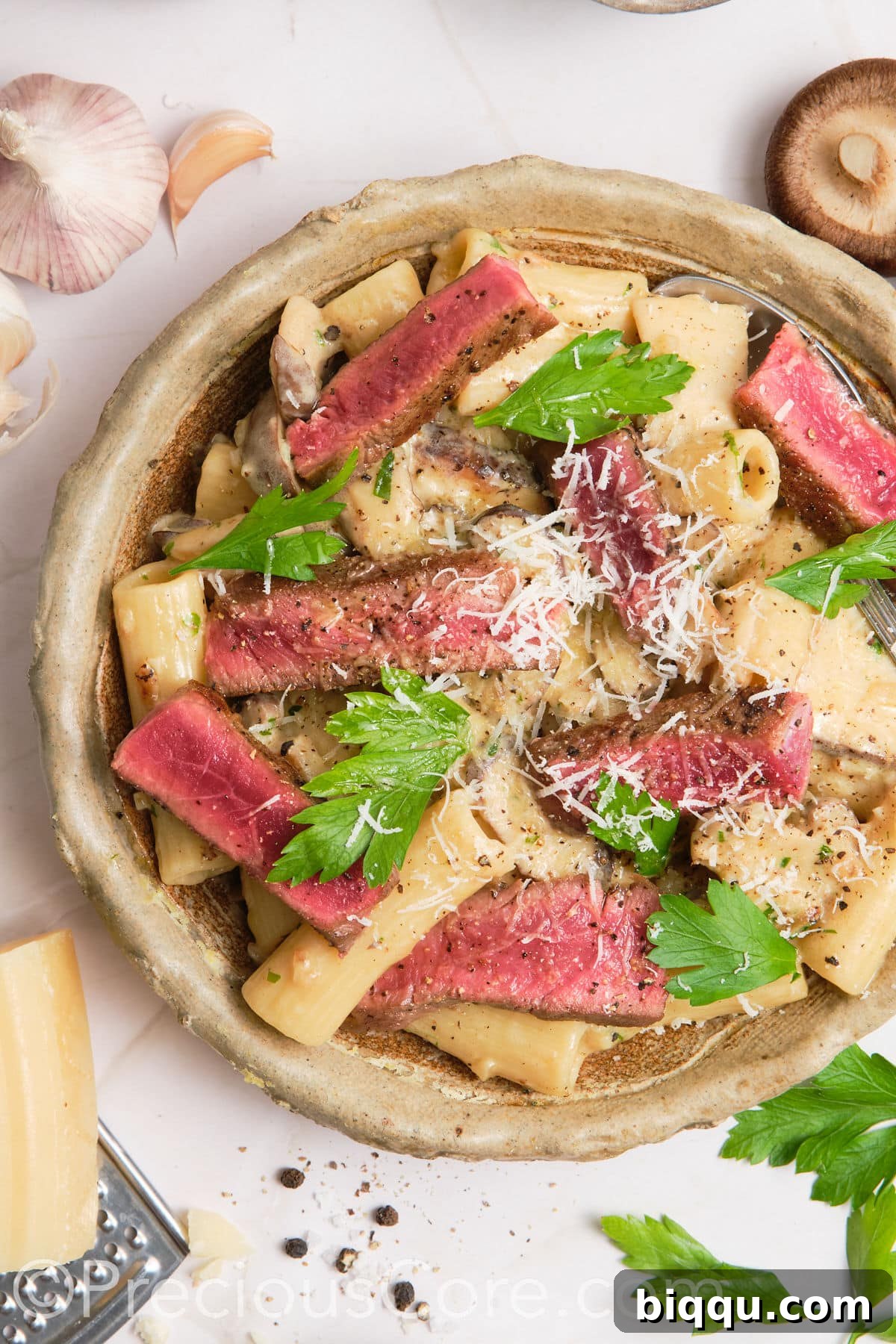 Creamy pasta in a bowl topped with juicy steak.
