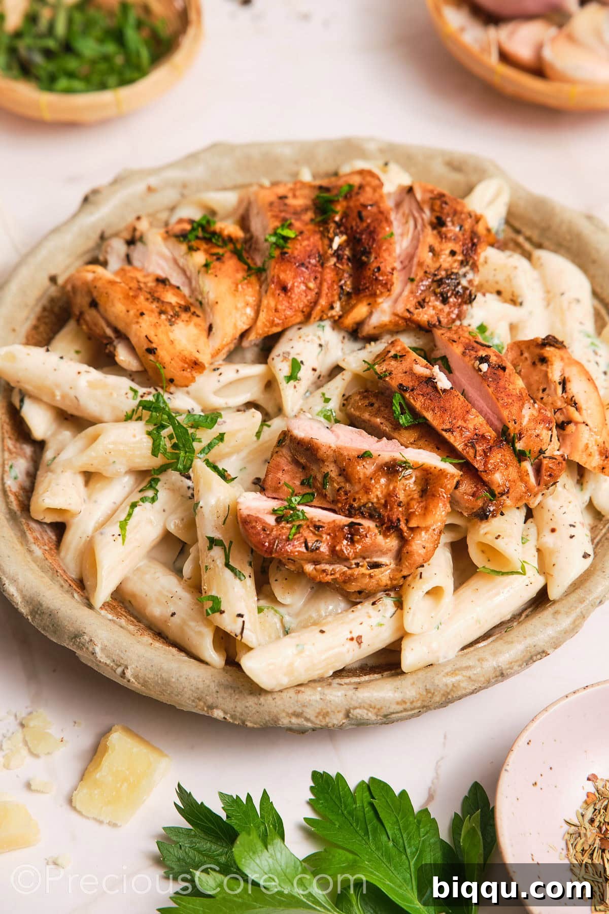 Creamy pasta in a bowl, topped with pan-seared chicken, garnished with fresh herbs.