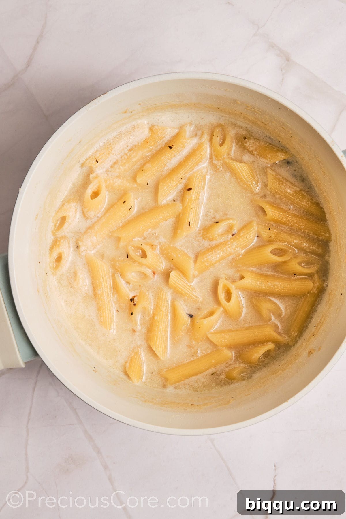 Penne pasta freshly added to the creamy liquid, beginning to cook and absorb the flavors.