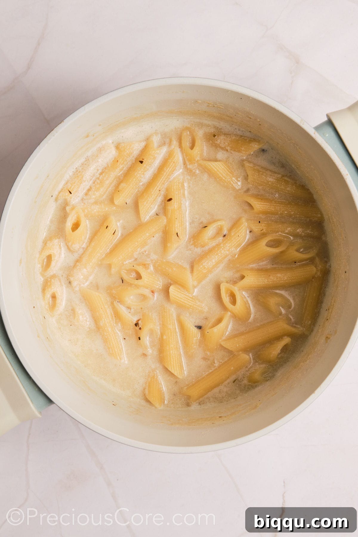 Penne pasta having absorbed most of the creamy liquid, becoming tender and coated.