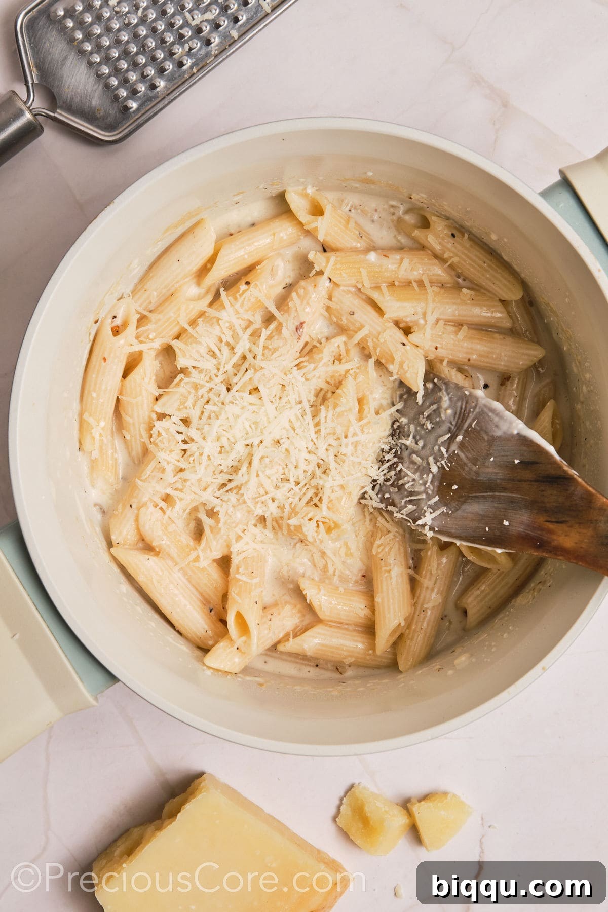 Shredded Parmesan cheese being added to the pot of creamy pasta, ready to be stirred in.