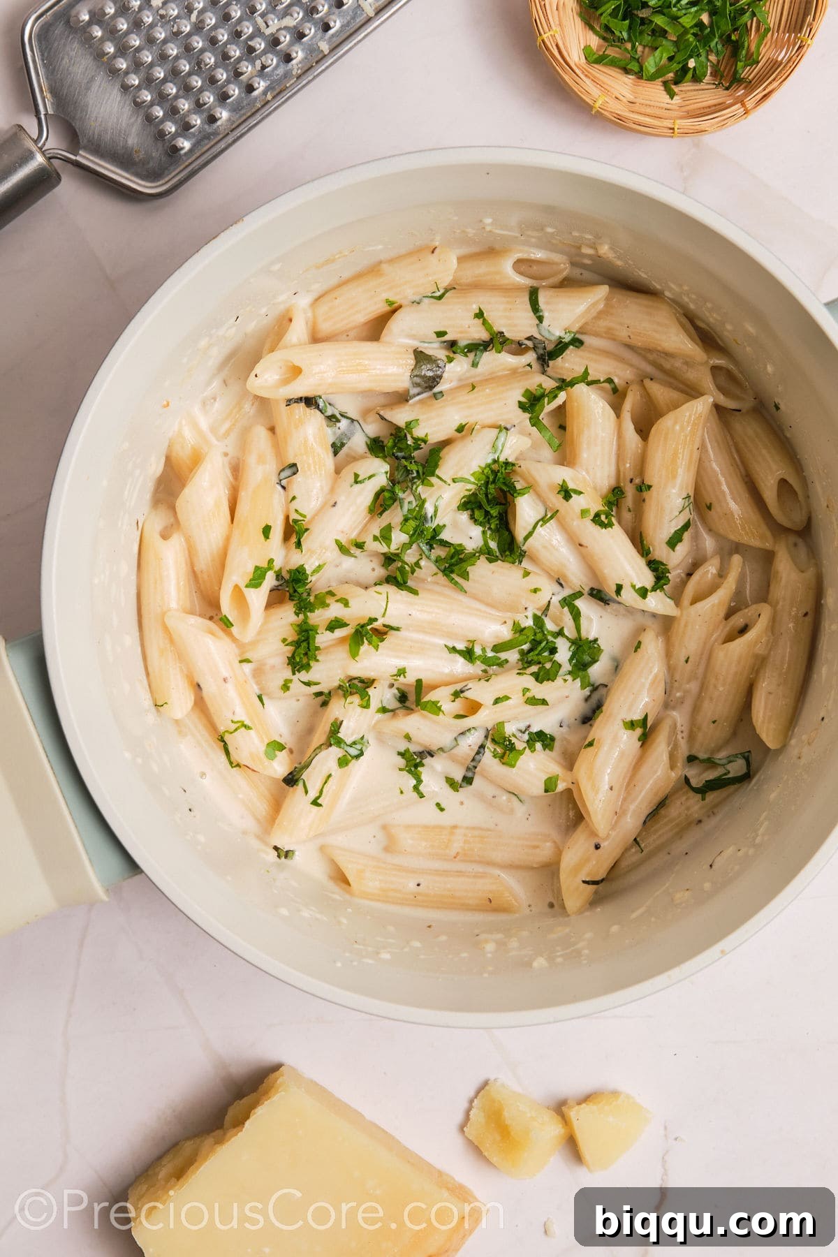 Fresh basil and parsley being stirred into the creamy pasta, adding color and aromatic notes.