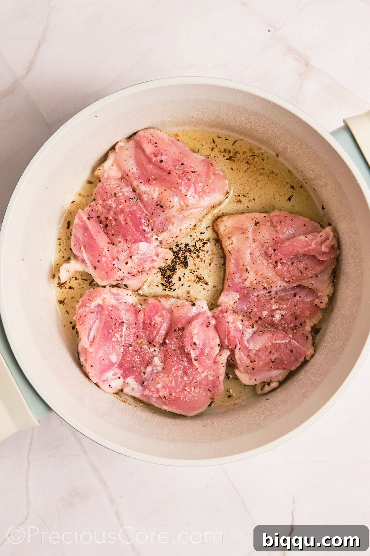 Boneless chicken thighs beginning to cook in a large pot, sizzling in hot olive oil.