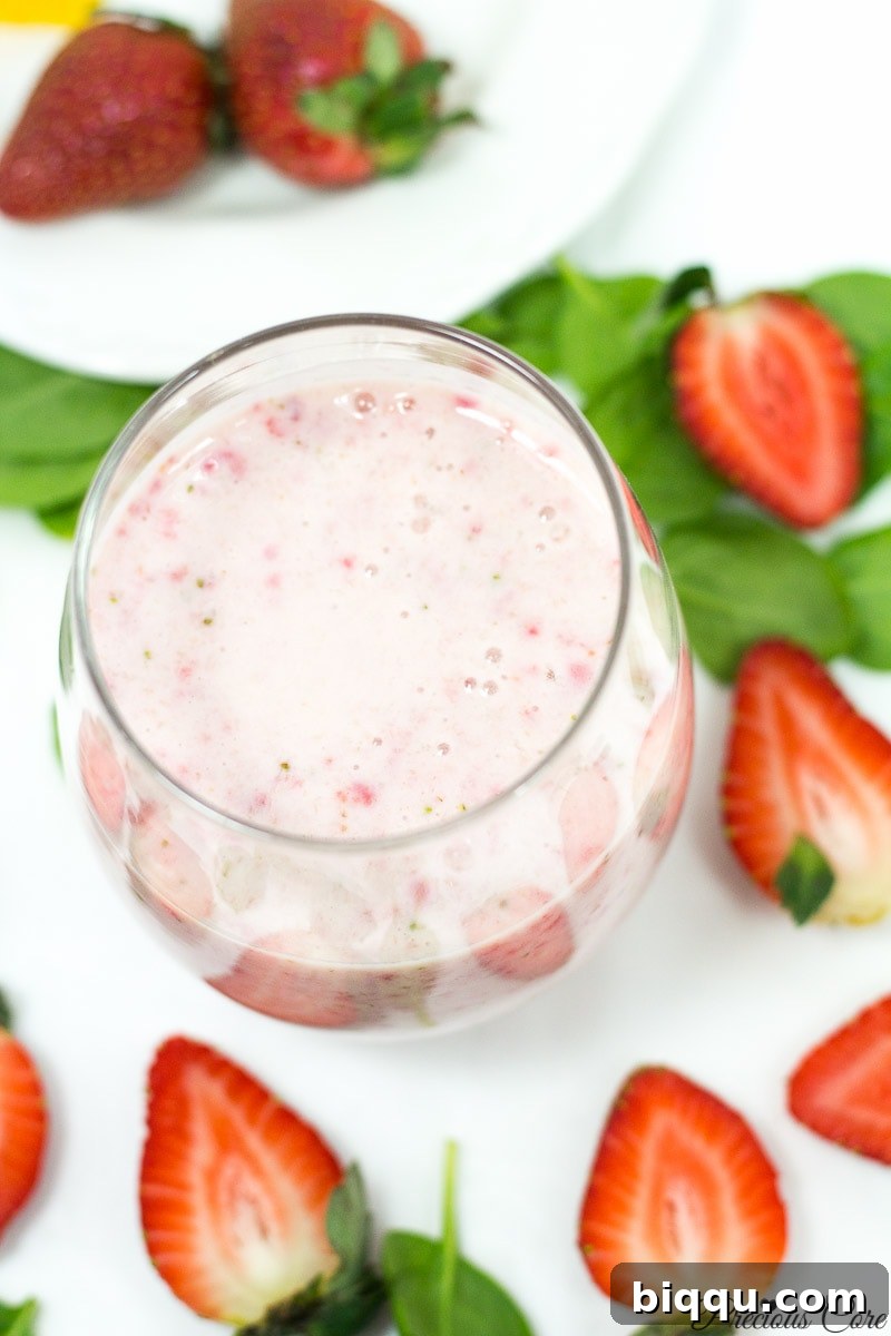 A creamy pink strawberry banana smoothie, topped with a fresh strawberry, served in a small clear glass.