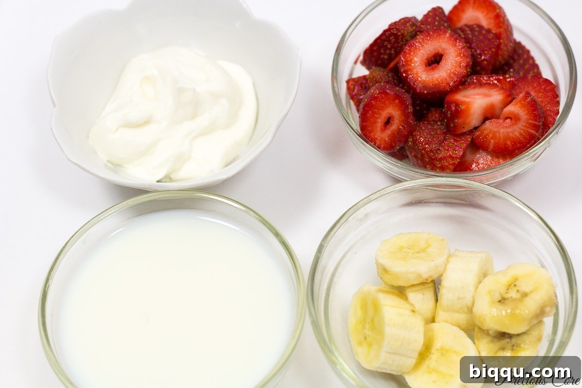 Strawberry-banana smoothie ingredients laid out: fresh strawberries, sliced banana, a cup of milk, and a bowl of yogurt.
