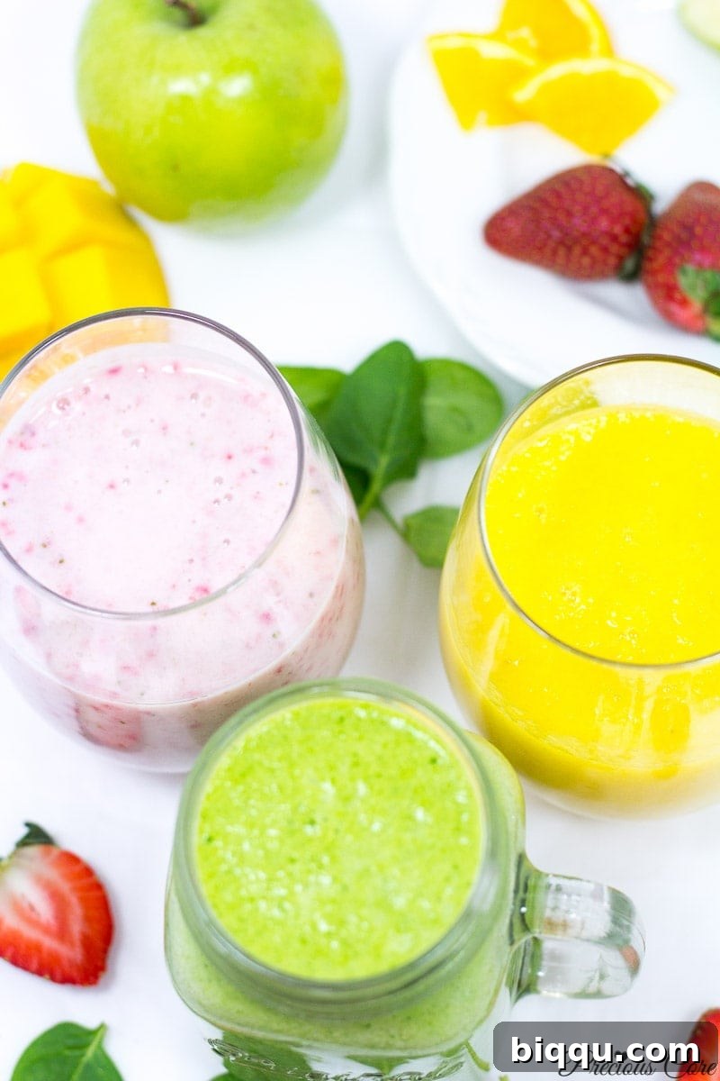 Three distinctly colored smoothies—yellow (pineapple-mango), green (spinach), and pink (strawberry-banana)—each in a small clear glass, arranged artfully on a light surface.