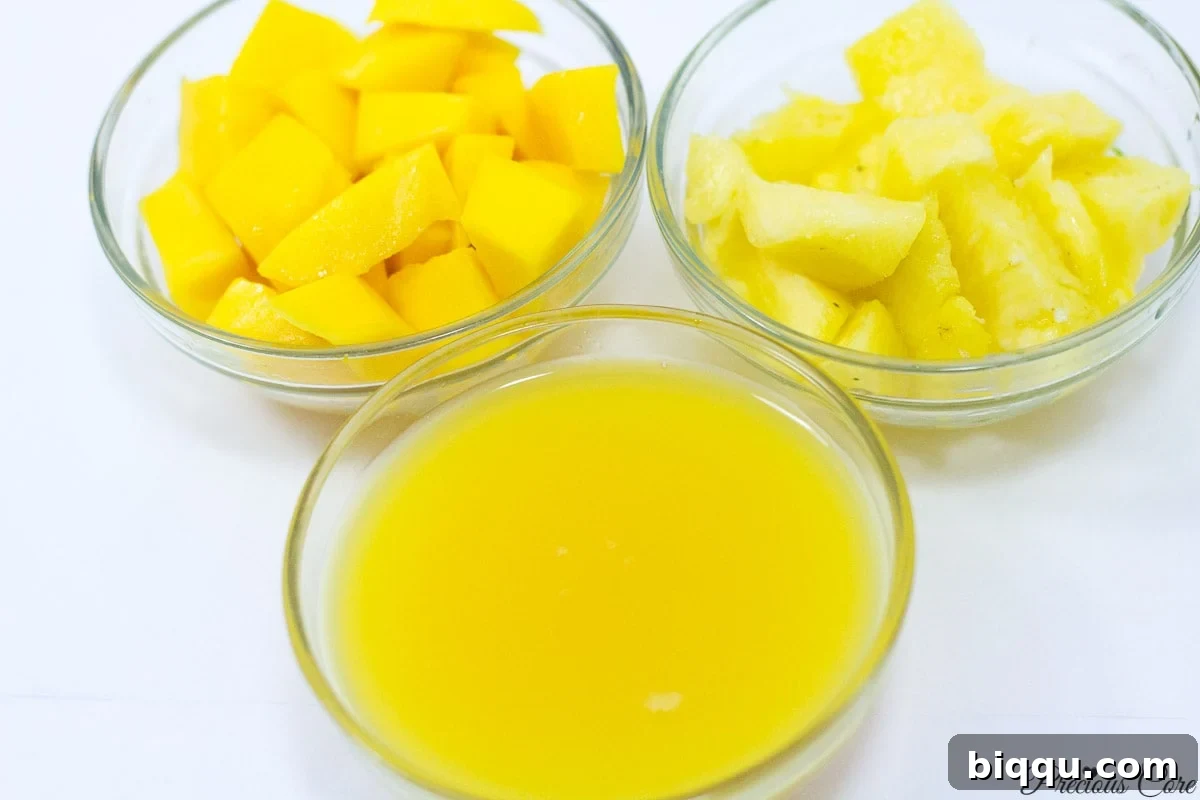 Three small bowls containing ingredients for a pineapple mango smoothie: chopped pineapple, chopped mango, and a glass of 100% orange juice.