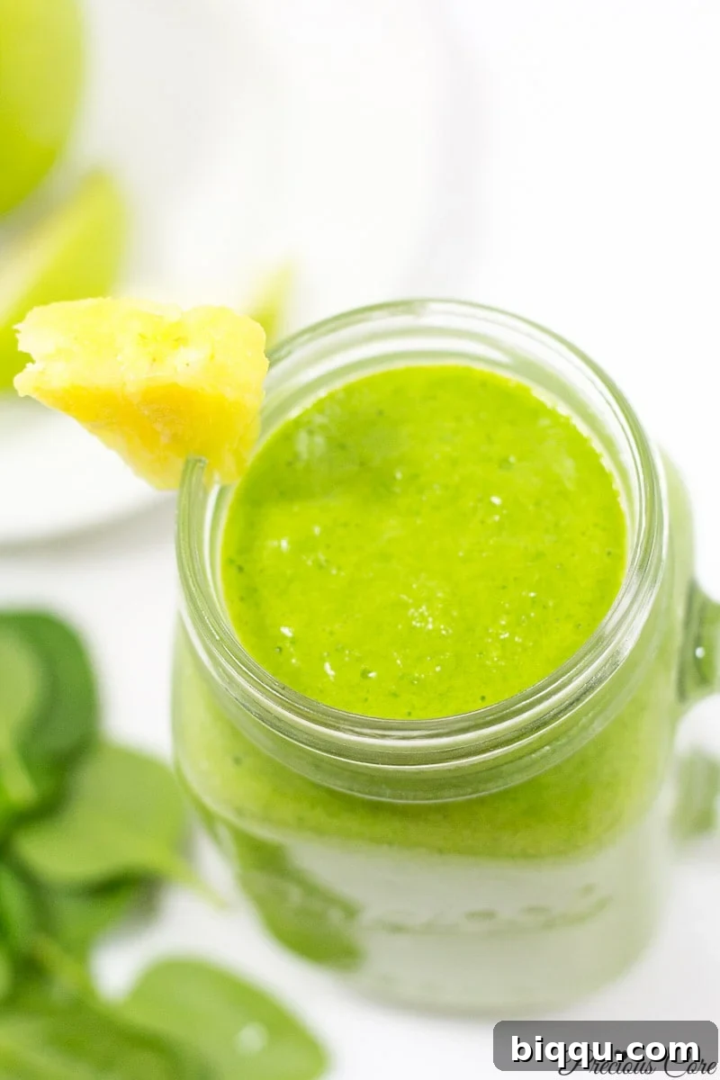 A vibrant green spinach smoothie in a clear glass, showing its healthy and refreshing texture, against a light background.