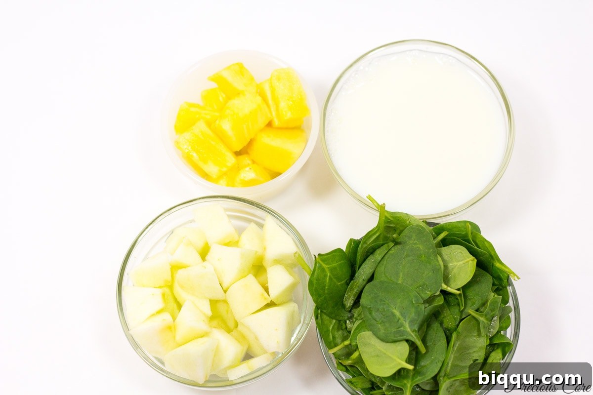 Close-up of green smoothie ingredients: fresh spinach, chopped green apples, chopped pineapple, and a glass of plant-based milk.