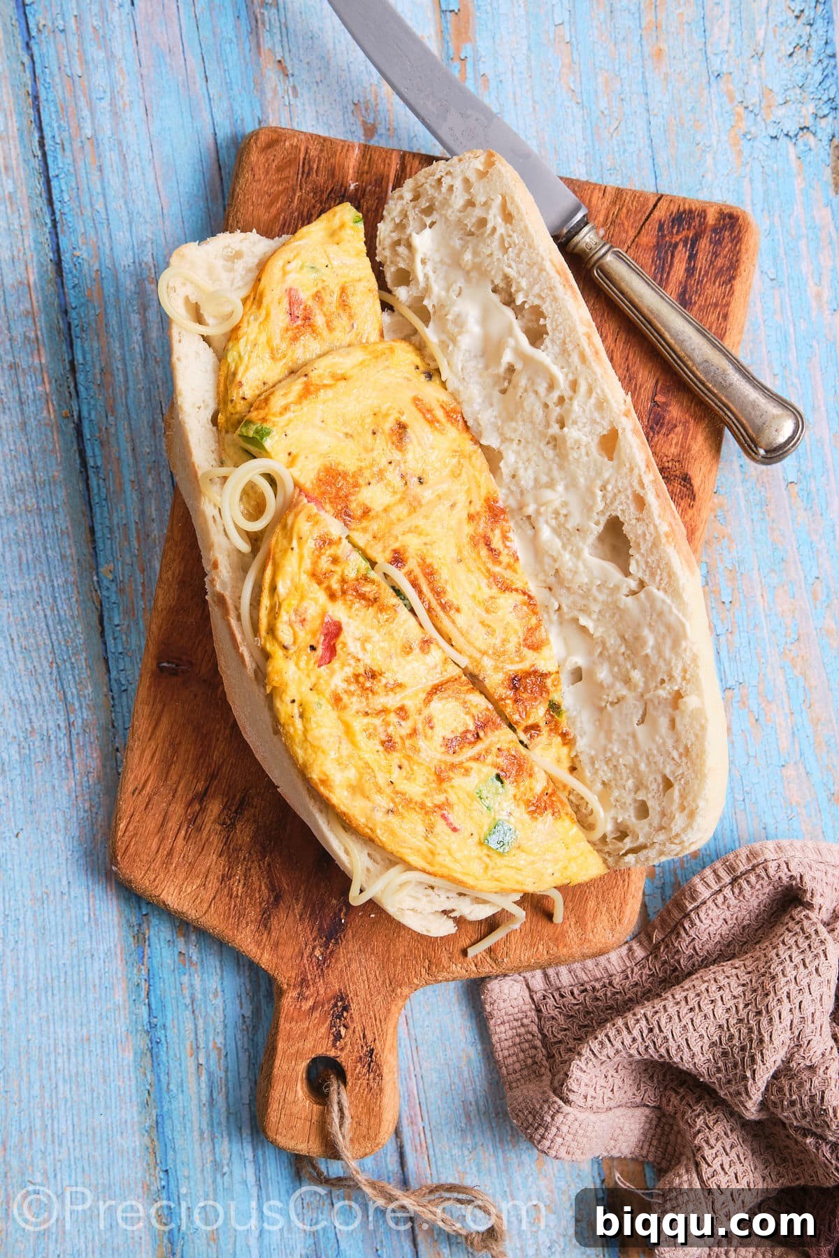 Slices of the savory spaghetti omelette carefully placed onto one side of an open French baguette, beginning the sandwich assembly.