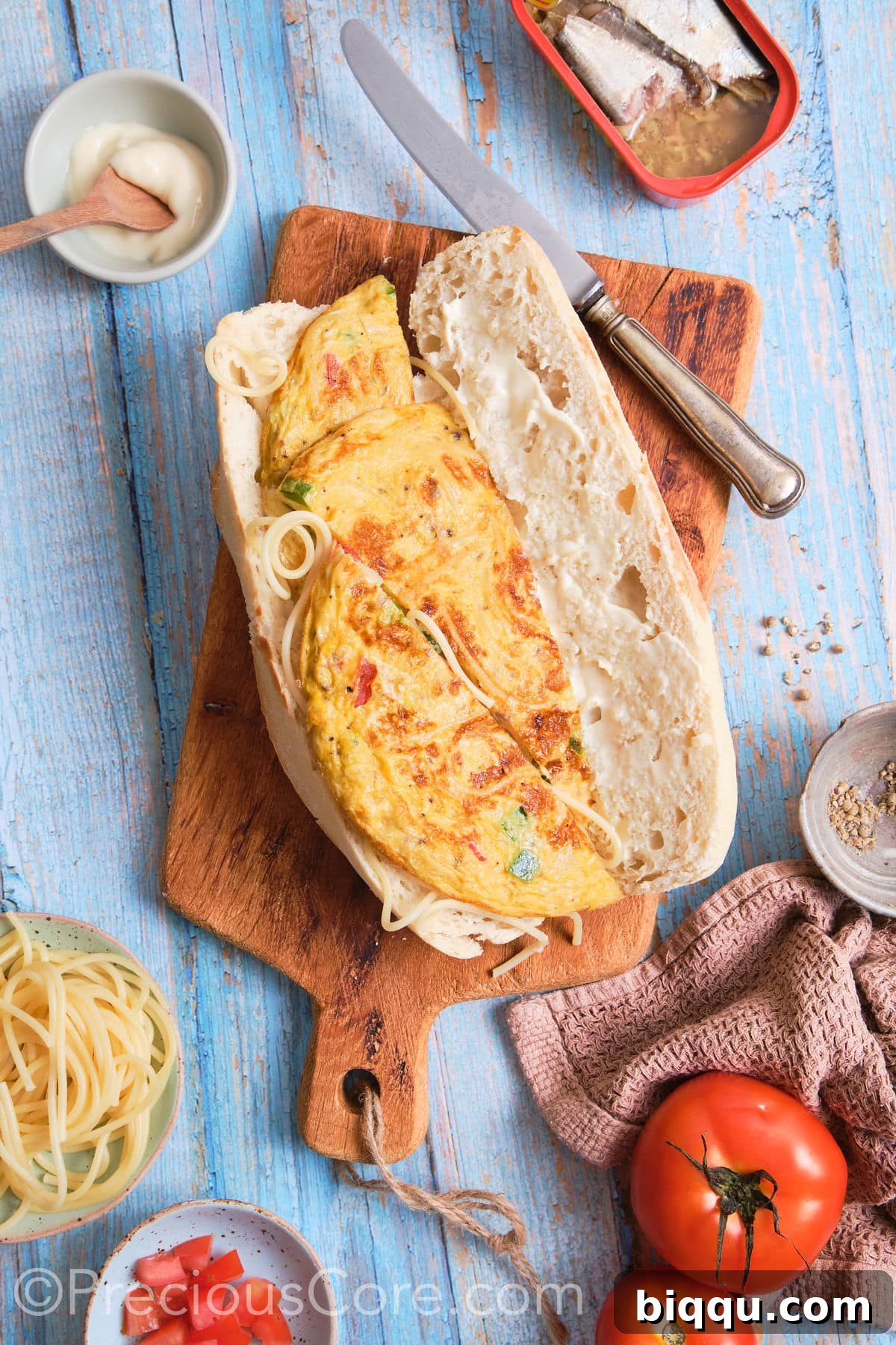 A French baguette carefully opened and laid flat, with one side generously filled with a vibrant, cooked spaghetti omelette, ready for assembly.