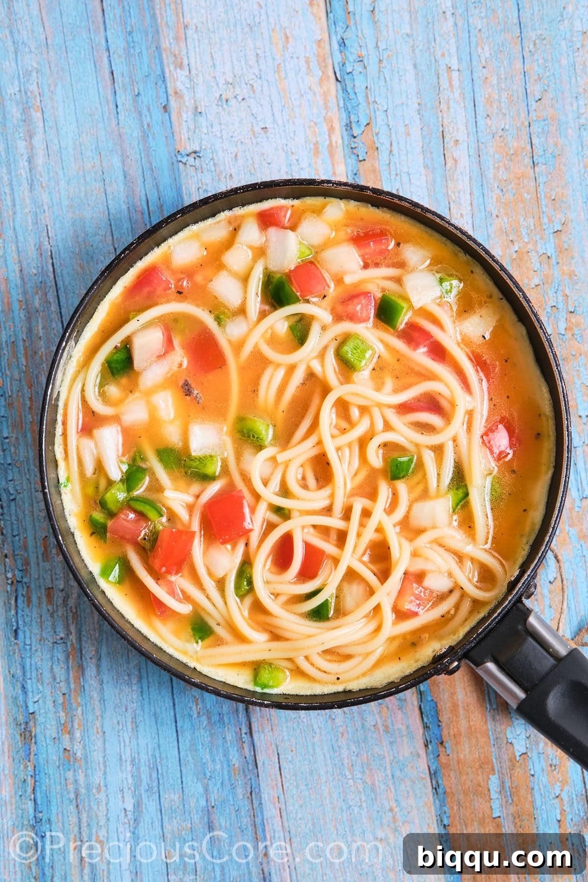 A savory spaghetti omelette cooking gently in a medium-sized non-stick skillet, covered, allowing the eggs to set and flavors to meld.