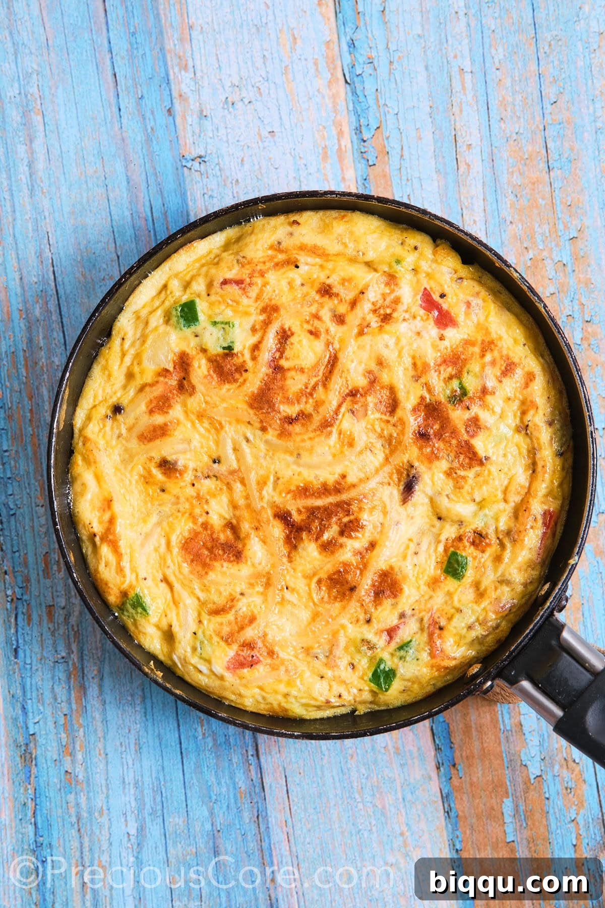The spaghetti omelette perfectly flipped in the skillet, displaying a golden-brown underside, continuing to cook to completion.