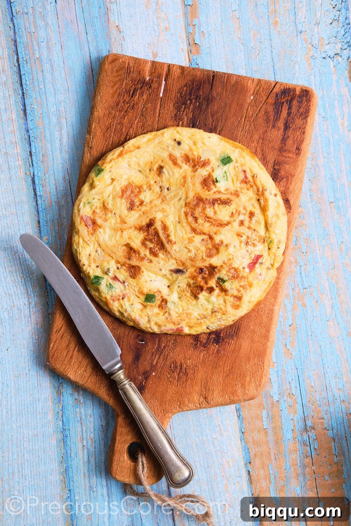 A freshly cooked spaghetti omelette resting on a cutting board, ready to be sliced and placed into the baguette.