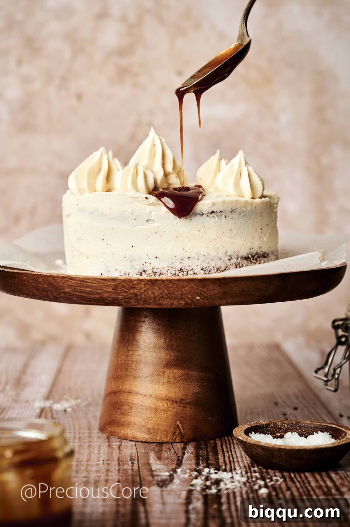 Adding a final touch of caramel drizzle and sea salt flakes to the top of the frosted salted caramel cake, enhancing both flavor and presentation.