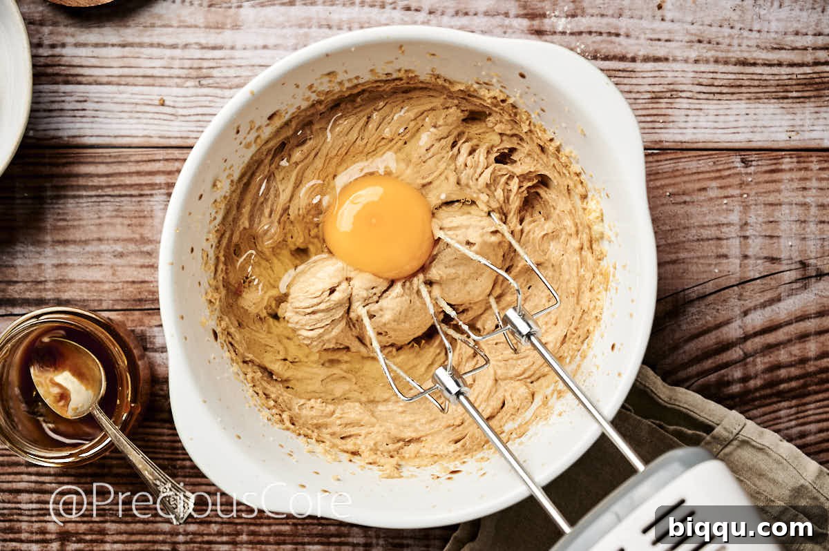 An egg being carefully cracked into the creamed butter and sugar mixture, ready to be incorporated for a smooth cake batter.