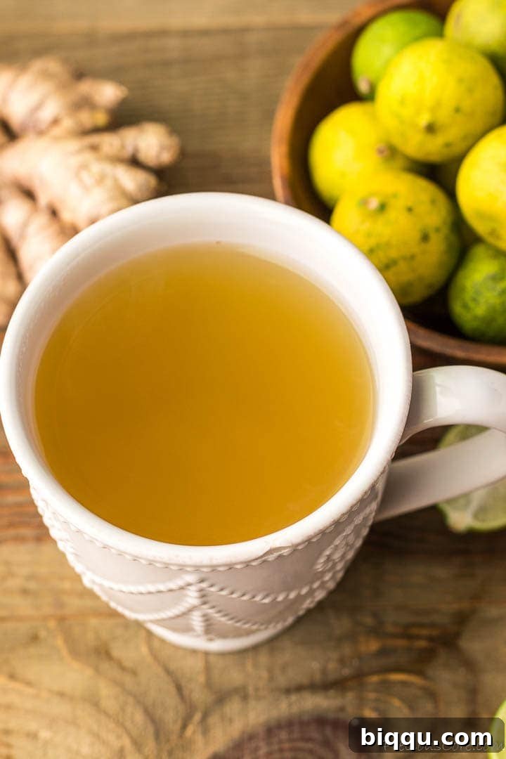 A mug of fresh ginger drink with some ginger and key limes on the side, emphasizing its refreshing and healthful nature.