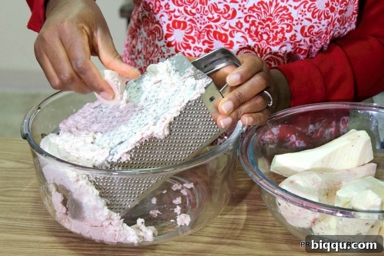 A close-up view of cocoyam being grated on a traditional box grater, demonstrating the manual preparation method.