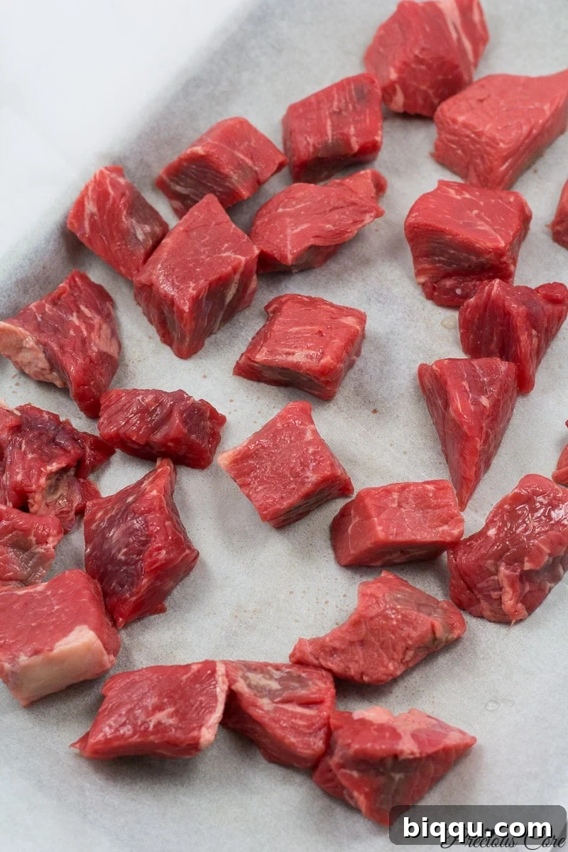 Cubed beef on a lined baking sheet, ready for oven smoking.