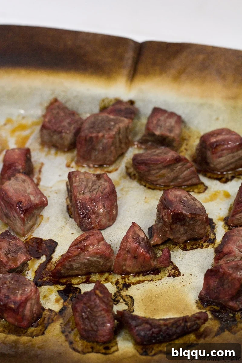 Cooked, oven-smoked beef cubes on a lined baking sheet, showing a rich brown color.