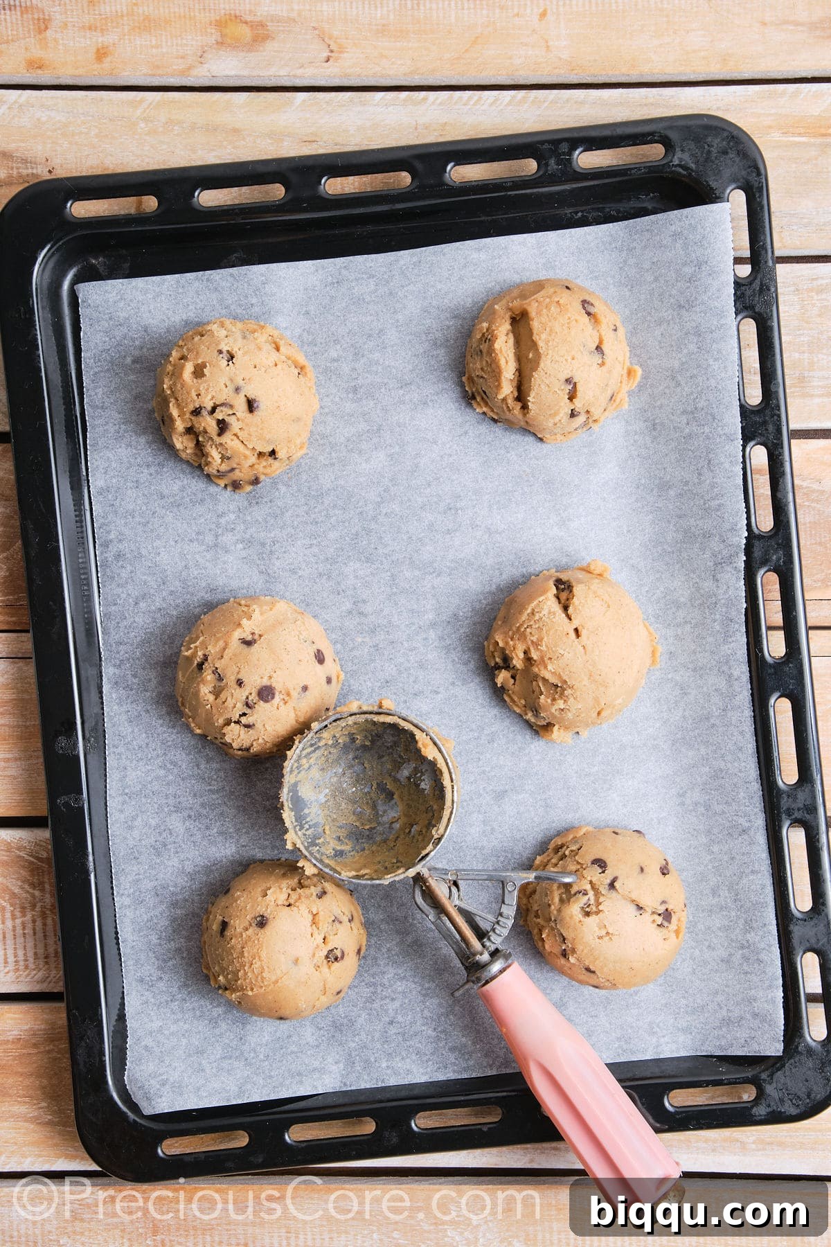 A baking sheet neatly lined with parchment paper, holding six perfectly scooped balls of cinnamon chocolate chip cookie dough, spaced appropriately for optimal baking and spread.