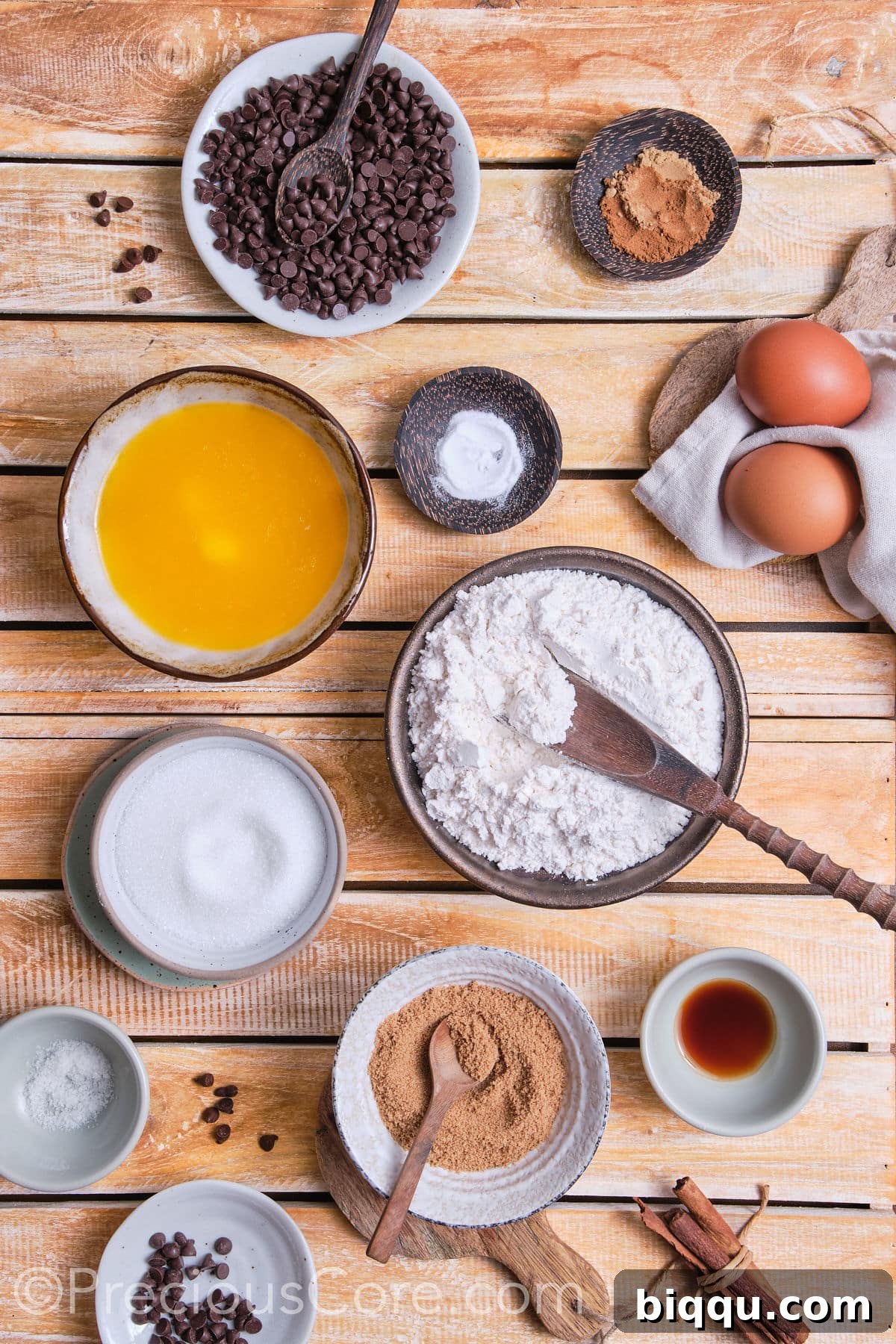 A selection of essential ingredients for making cinnamon chocolate chip cookies, including flour, sugar, butter, eggs, cinnamon, ginger, and chocolate chips, meticulously arranged on a kitchen counter.