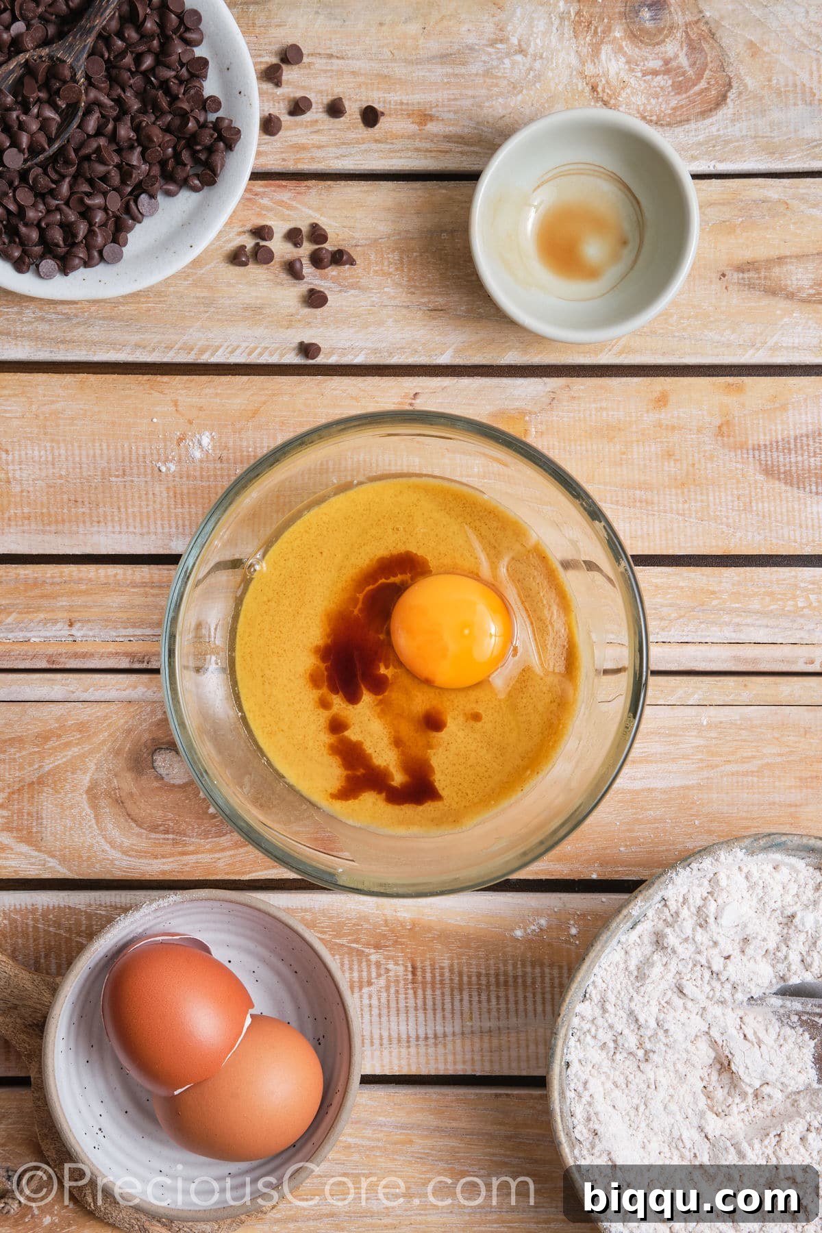 Adding an egg and vanilla extract to the creamed butter and sugar mixture in a bowl, a vital step for enriching the cookie dough's flavor and structure.