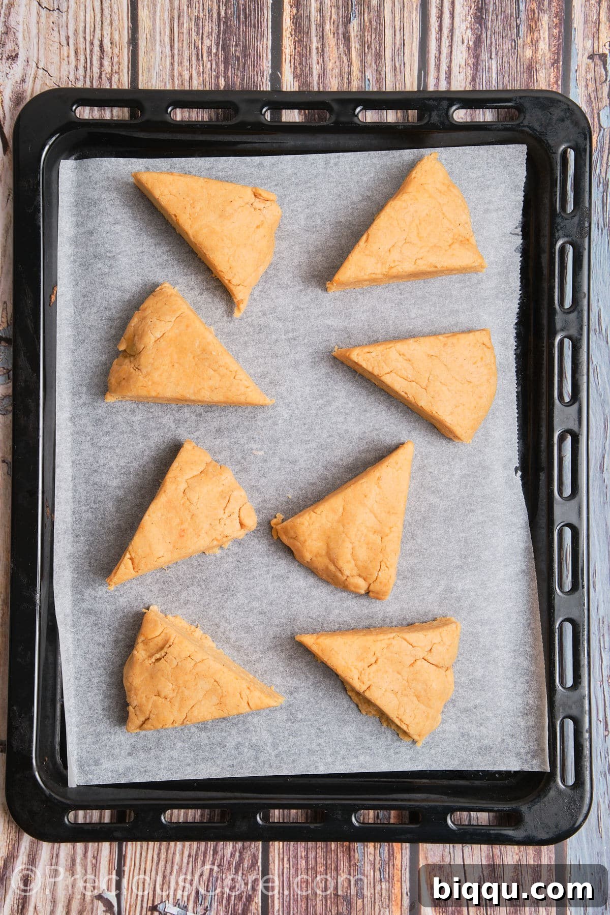 Triangles of unbaked scones placed neatly on parchment paper on a baking sheet.