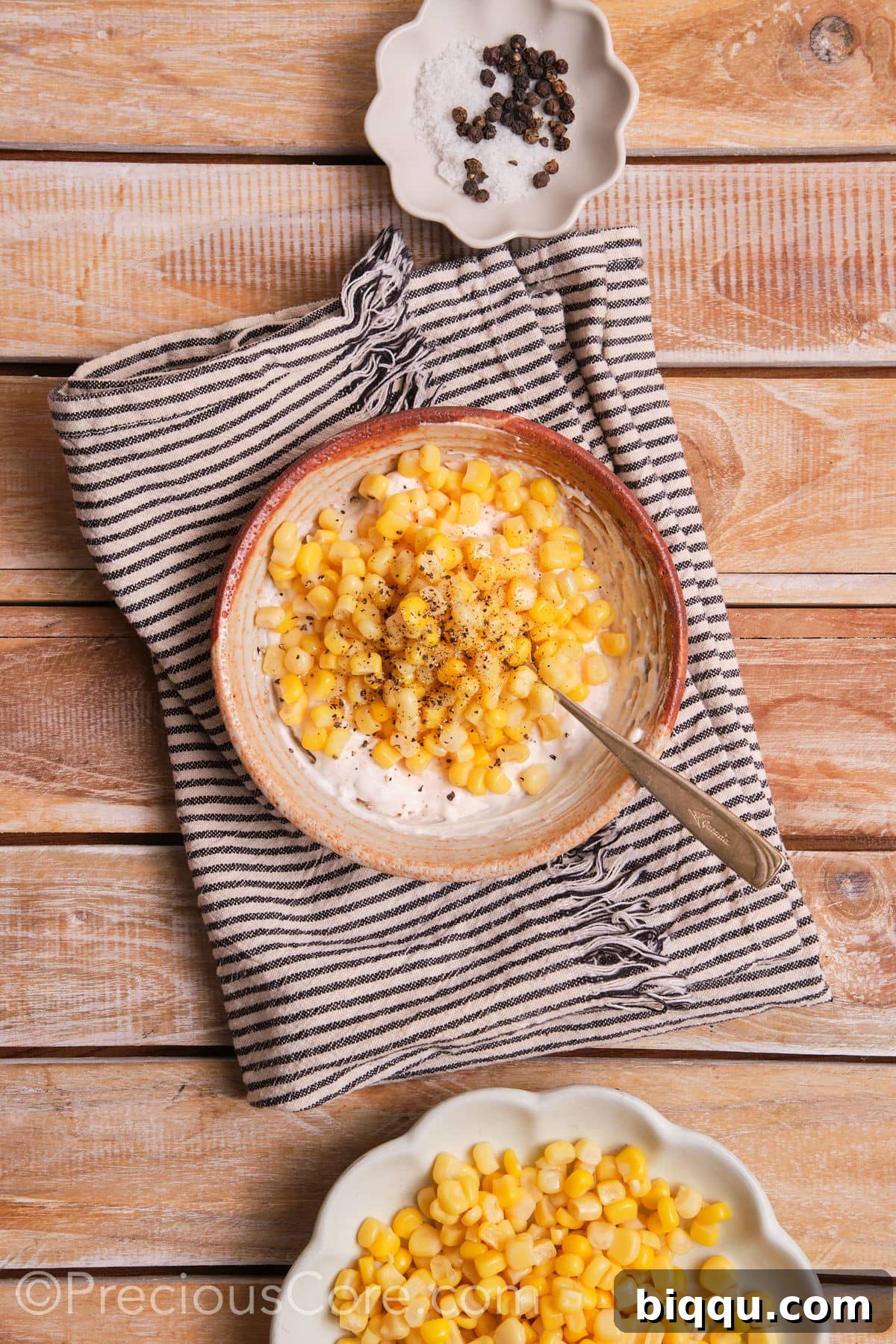 Thawed corn kernels being stirred into the creamy sauce in a bowl.